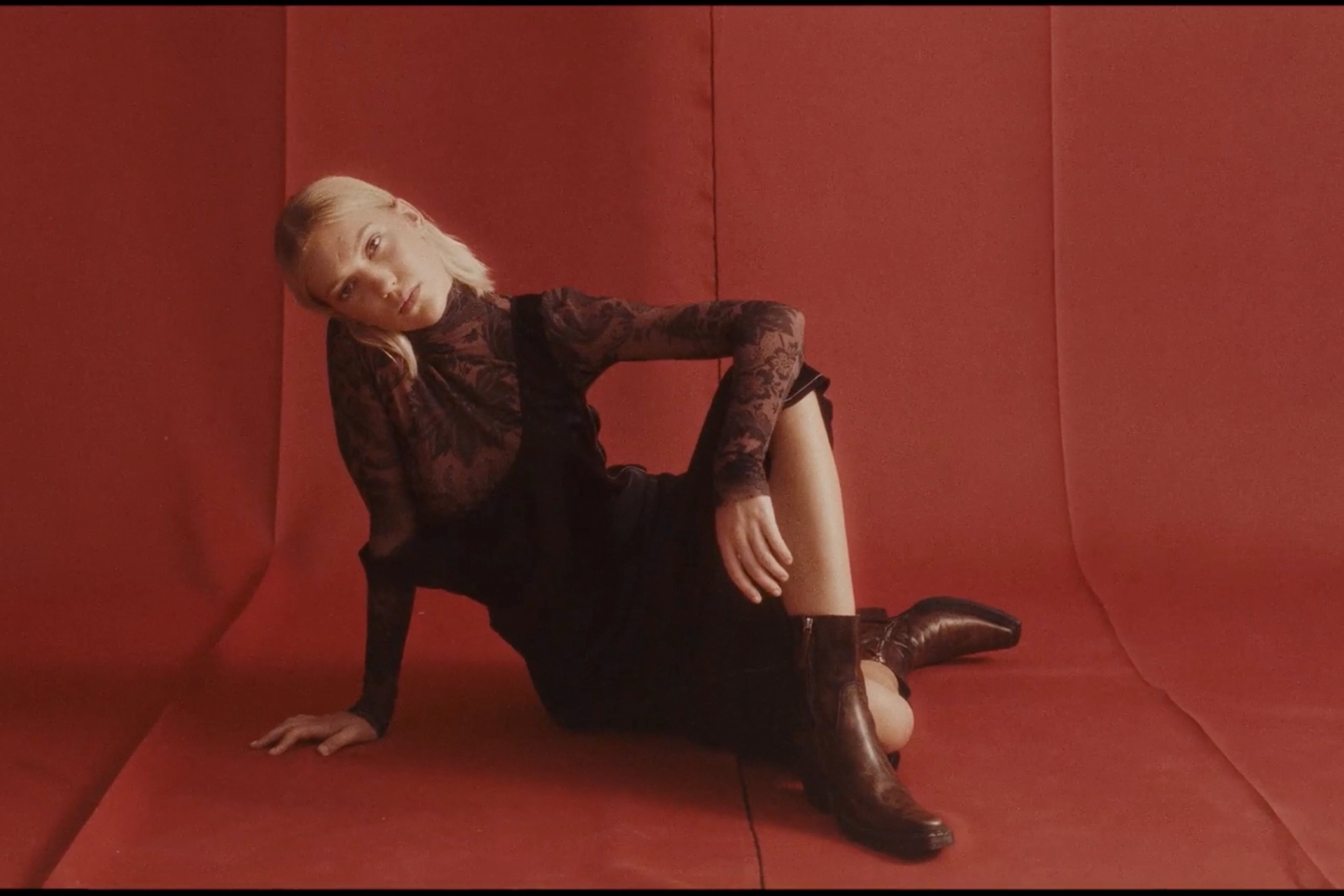 Photography of young woman sitting on a red studio backdrop.